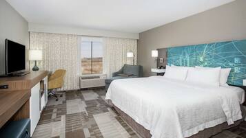 A hotel room with a large bed, a desk with a computer, a chair, a TV, and a window with curtains.