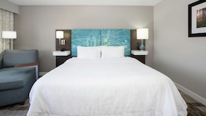 Ett hotellrum med en stor säng, en blå, abstrakt väggdekoration, två sänglampor, ett sidobord och en blå fåtölj.
