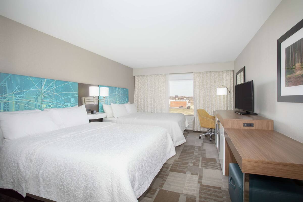 A hotel room with two beds, a desk, a television, and a window with a view.