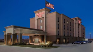 Ett Hampton Inn-hotell med en flagga på taket, en överbyggd entré och en parkeringsplats.