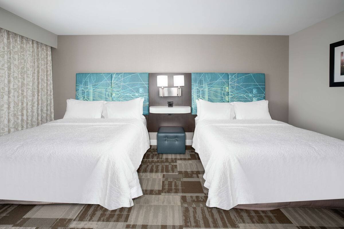 A hotel room with two beds, a small bathroom, and a decorative headboard.