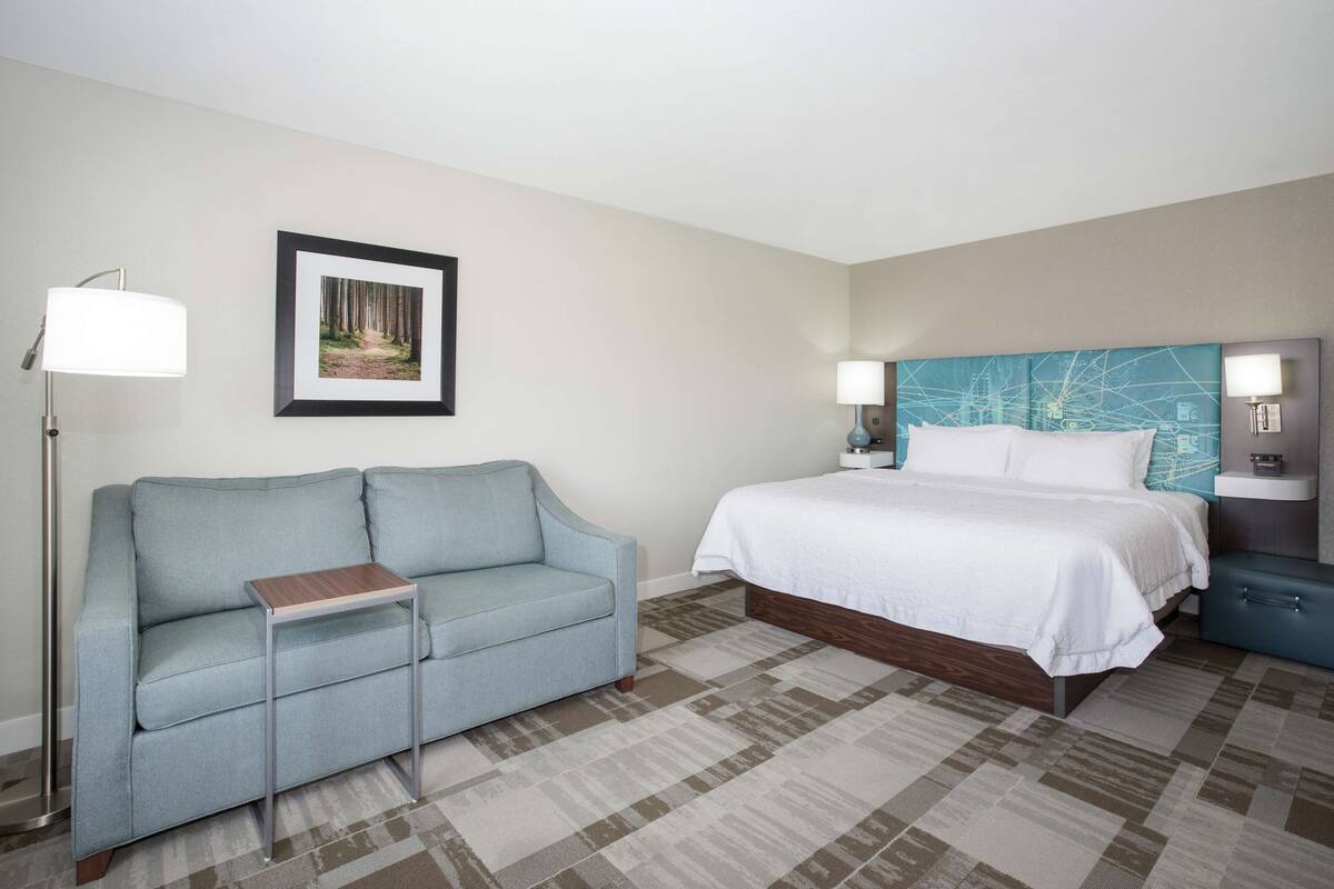 A hotel room with a bed, a sofa, a small table, and a framed picture on the wall.