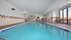 En inomhuspool med kristallklart blått vatten, kaklade väggar och ett rutmönster längs poolens kant. Det finns stolar och ett litet bord i närheten av poolen, och en dörr som leder till ett annat rum.