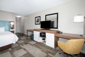 A hotel room with a bed, a desk with a television, a chair, a microwave, and a coffee maker.