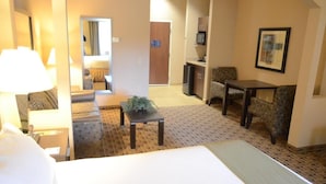 Une chambre d’hôtel avec un lit, une petite table avec une plante, une chaise, un bureau et un four à micro-ondes.