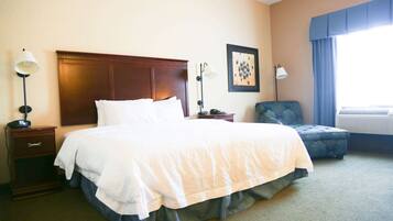 A hotel room with a large bed, a nightstand with a lamp, a chair, and a window with curtains.