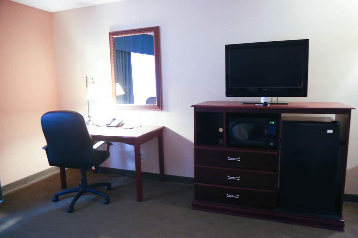 A hotel room with a desk, office chair, television, and a minibar.