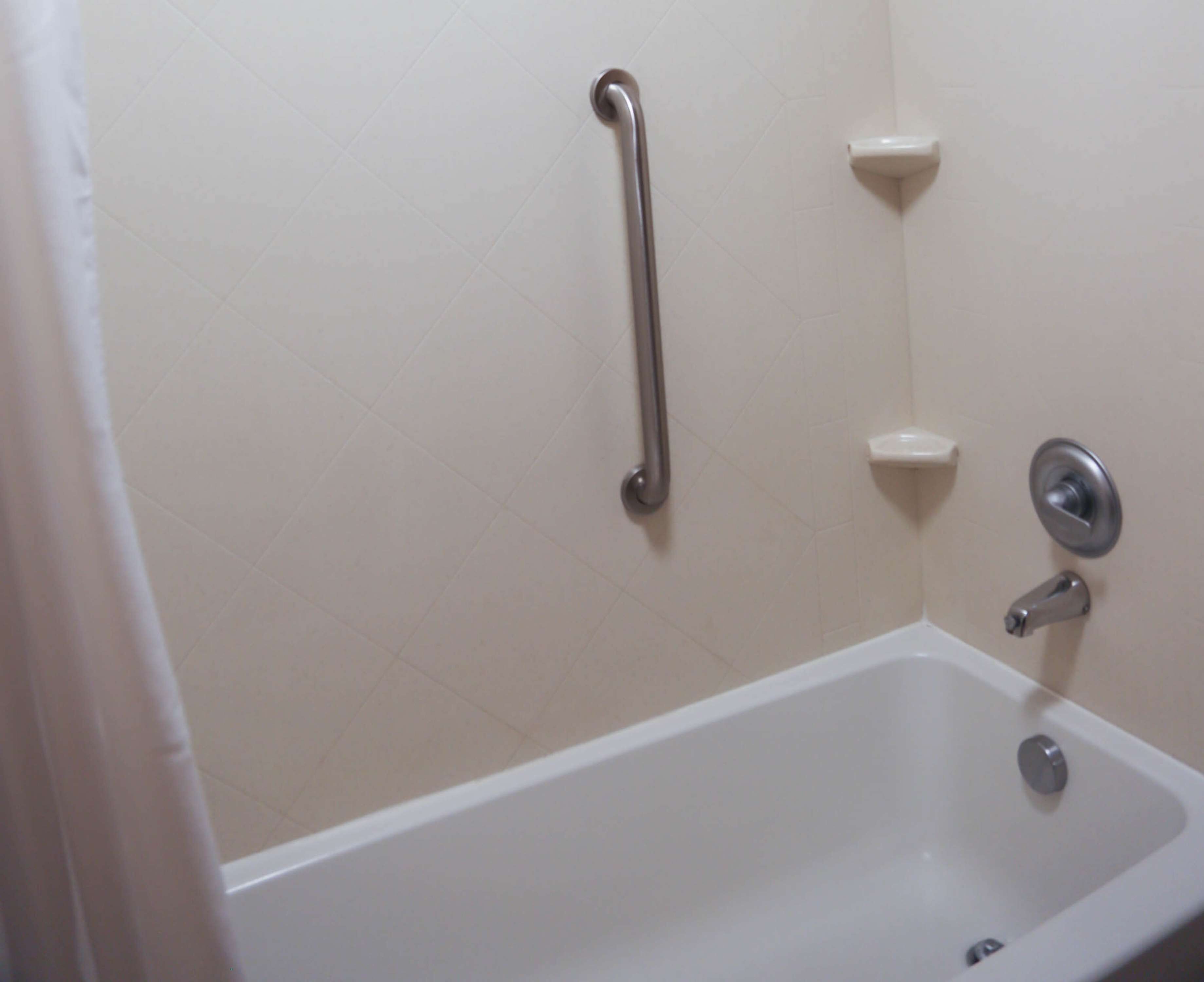 Un bagno con una vasca, un mancorrente e un piccolo ripiano.