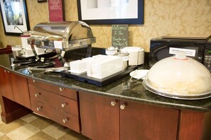 A buffet setup with a coffee station, a microwave, and a sign welcoming guests to the Hampton Inn.