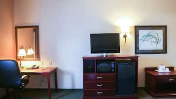 Habitación de hotel con escritorio, silla, televisor, microondas y un mueble pequeño.