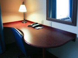 Una habitación de hotel con escritorio, teléfono, lámpara y espejo.