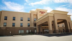 Un hotel Hampton Inn con fachada beige moderna, múltiples ventanas y cielo despejado.