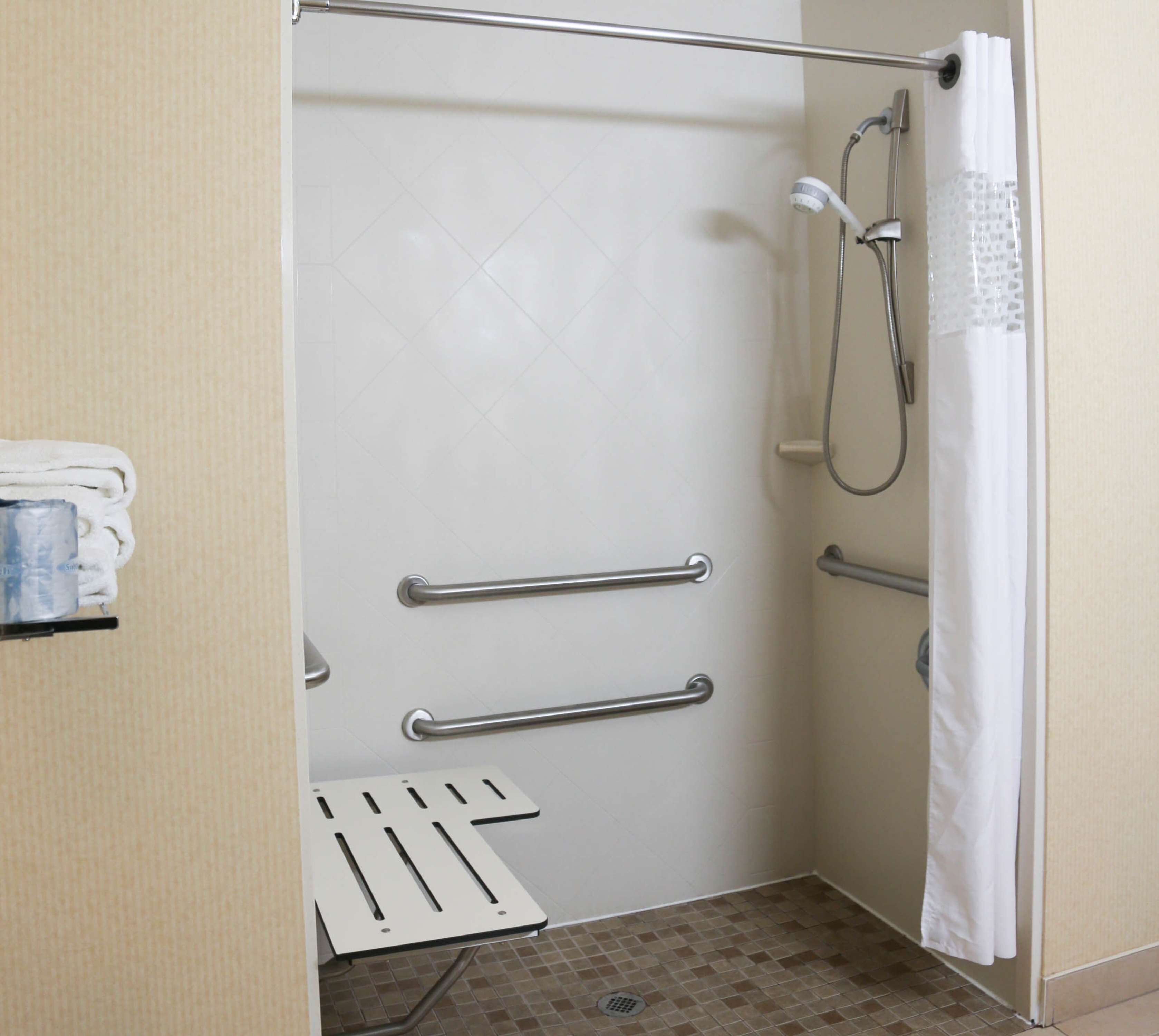 A bathroom with a shower, grab bars, and a towel rack.