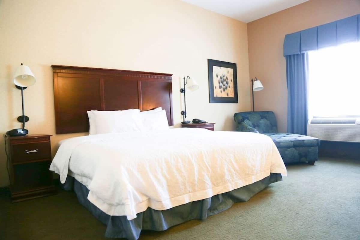 A hotel room with a large bed, bedside tables, a chair, a framed picture on the wall, and a window with curtains.