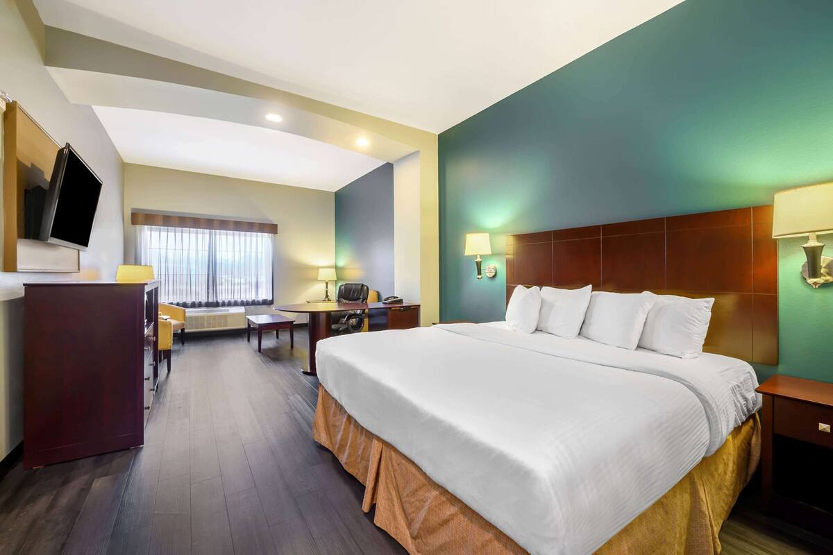 Ein Hotelzimmer mit einem großen Bett, einem Schreibtisch, einem Sessel, einem Fernseher und einem Fenster mit Vorhängen.
