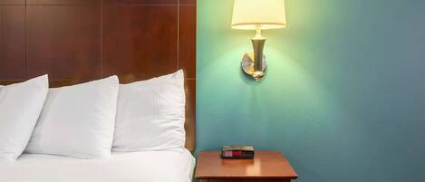 A hotel room with a neatly made bed, a bedside table with a lamp, and a small nightstand.