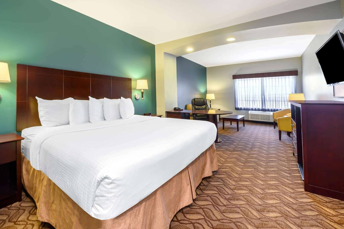 Ein Hotelzimmer mit einem großen Bett, einem Schreibtisch, einem Stuhl, einem Fernseher und einem fenster mit Vorhängen.