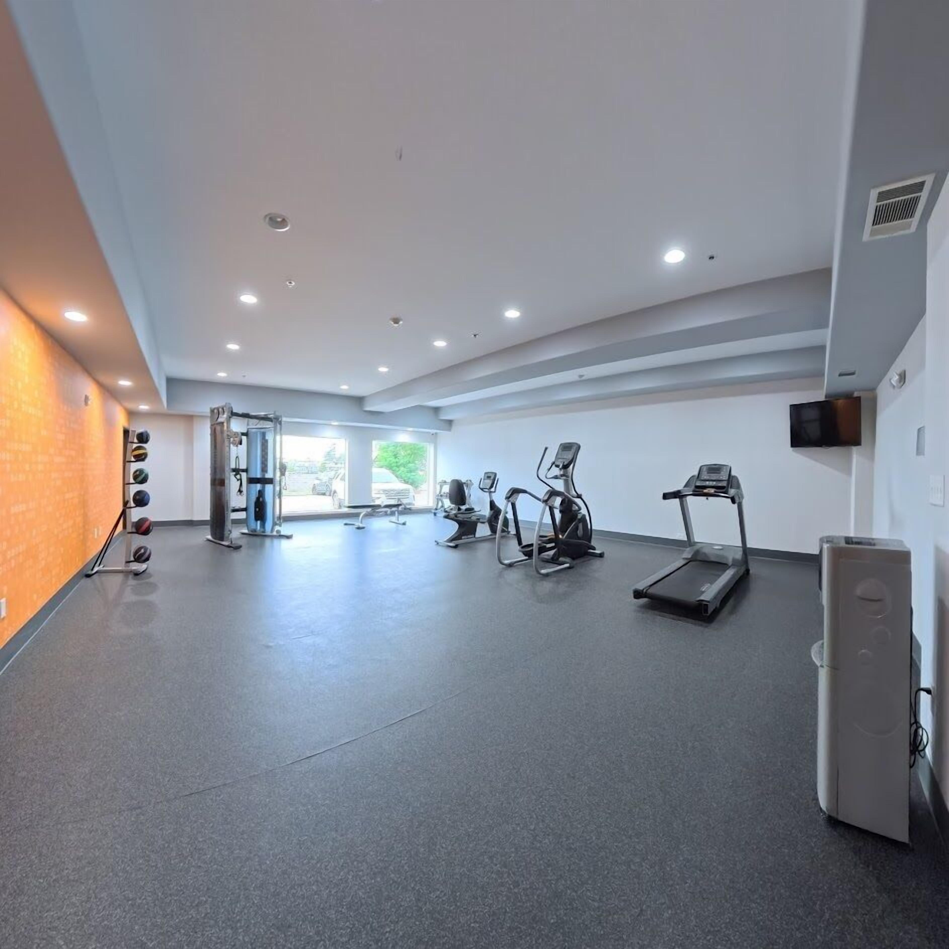 Une salle de sport moderne équipée de tapis de course, de vélos elliptiques et d’un ensemble de poids.