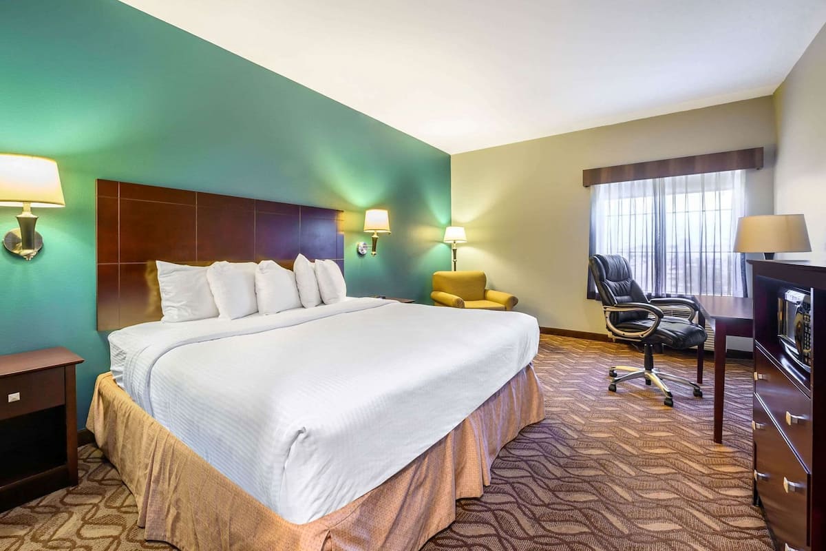 Ein Hotelzimmer mit einem großen Bett, zwei Nachttischlampen, einem Schreibtisch mit Stuhl und einem fenster mit Vorhängen.