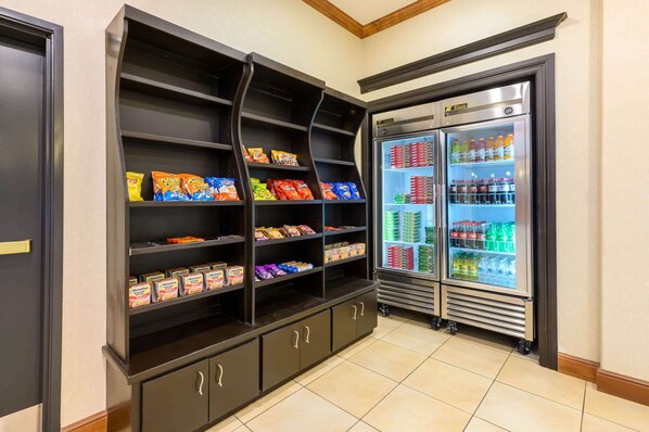 A snack shelf stocked with various packaged foods and a refrigerator filled with beverages. - La Quinta Inn & Suites by Wyndham Longview North (Longview)