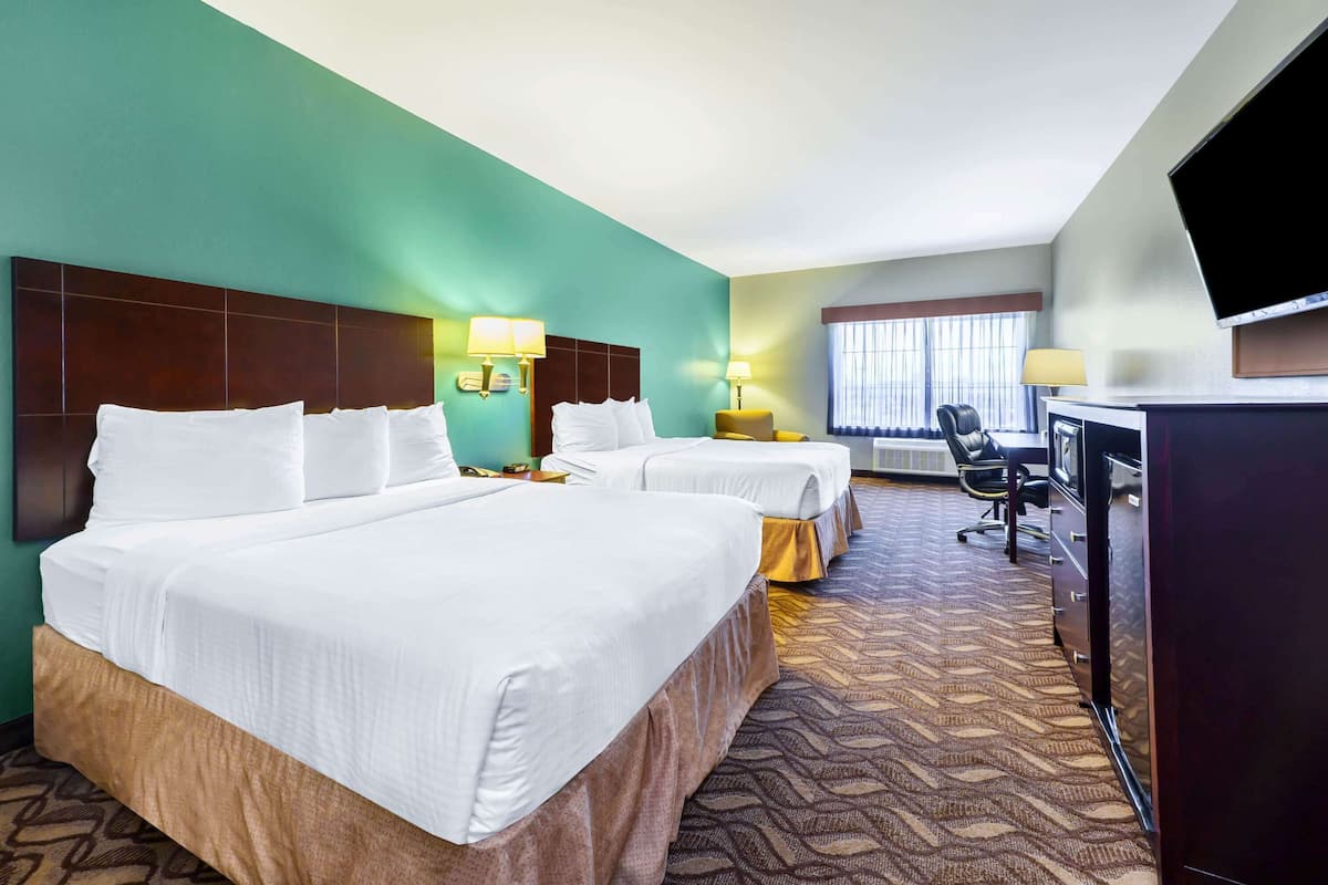 Ein Hotelzimmer mit zwei Betten, einem Schreibtisch, einem Stuhl, einem Fernseher und einem Fenster mit Vorhängen.