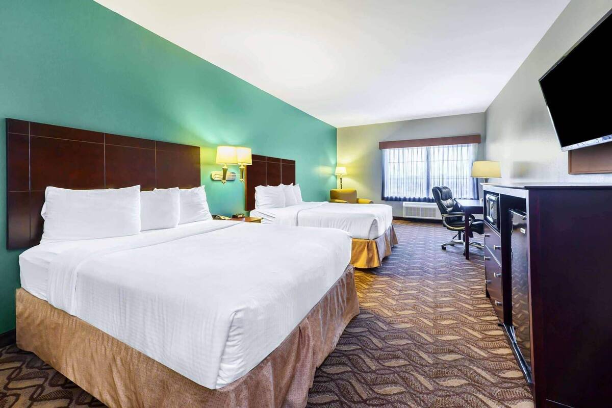 Ein Hotelzimmer mit zwei Betten, einem Schreibtisch, einem Stuhl, einem Fernseher und einem Fenster mit Vorhängen.