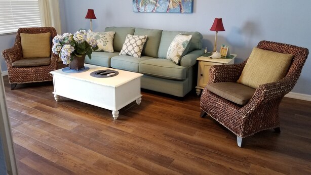 Een woonkamer met een lichtgroene bank, twee rieten fauteuils, een witte salontafel en een rode lamp op een nachtkastje.