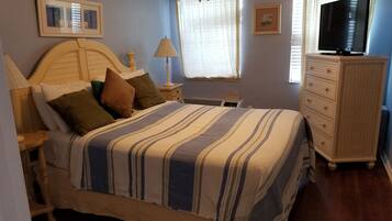 A bedroom with a bed, bedside tables, a dresser, a television, and framed pictures on the wall.
