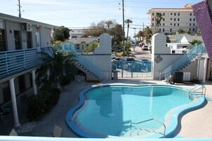 Una piscina con borde curvo, rodeada por una barandilla azul, junto a un edificio con una escalera que lleva a un balcón.