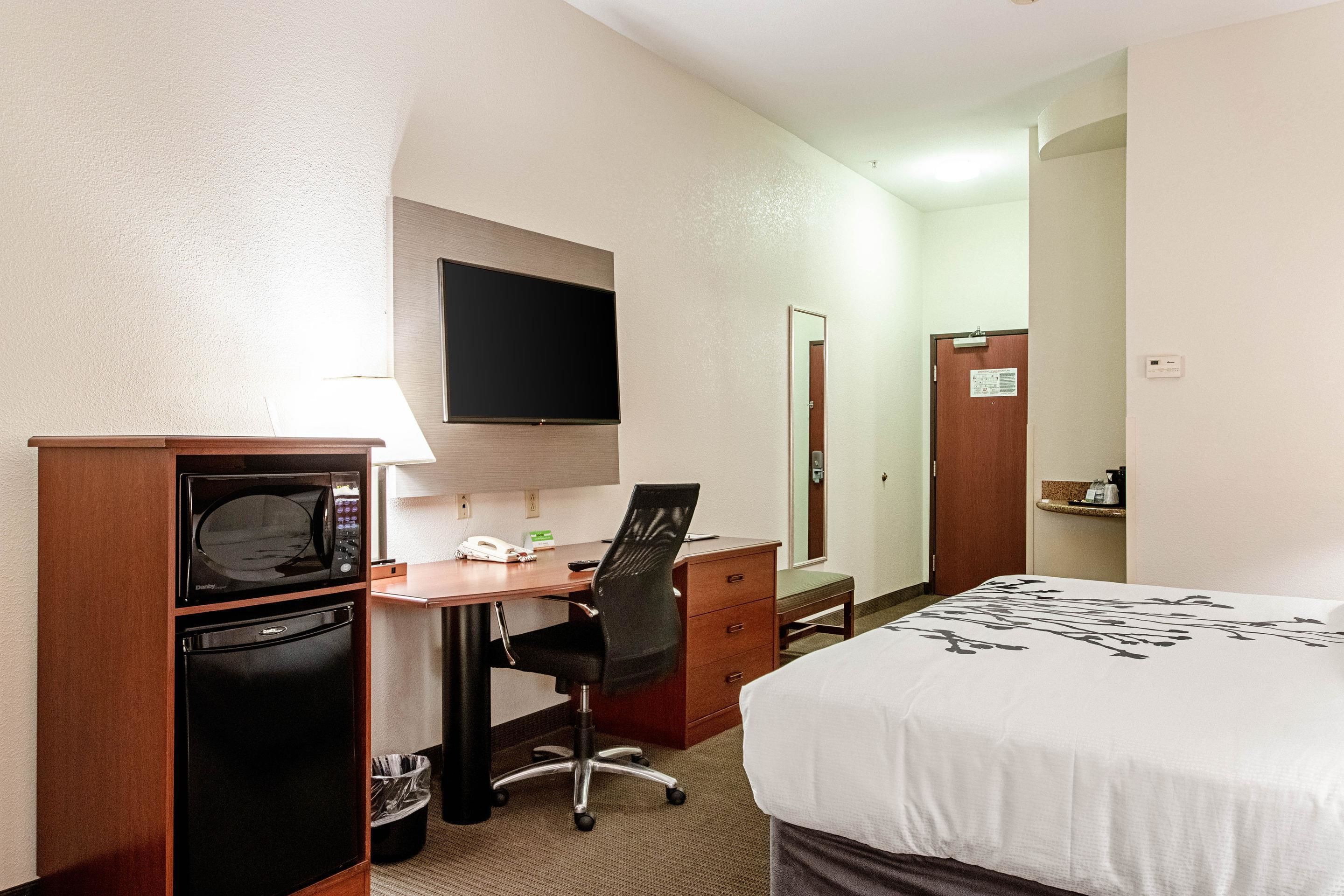 Una habitación de hotel con cama, escritorio con computadora, microondas y refrigerador.