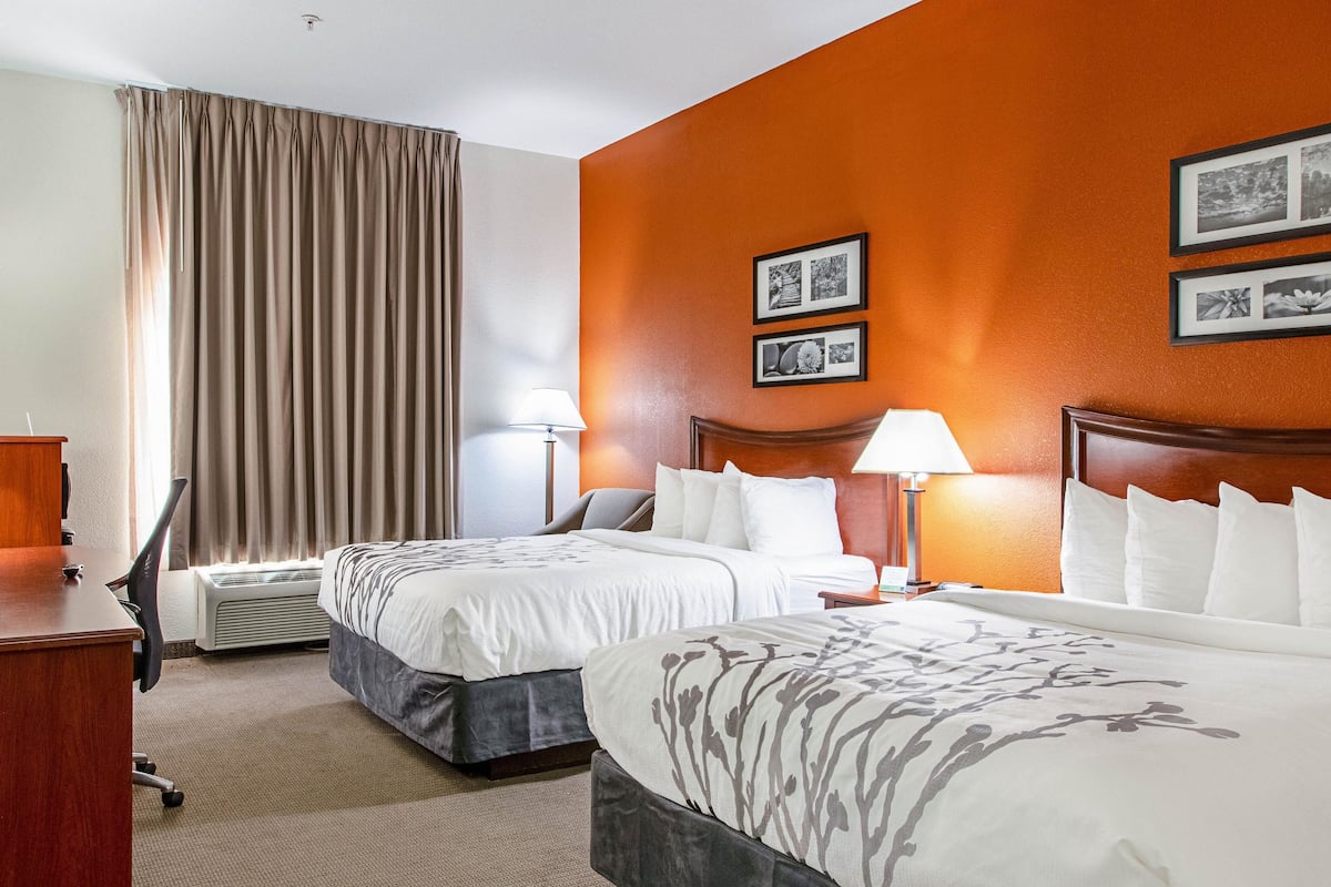 A hotel room with two beds, a desk, a chair, and a large window with curtains.