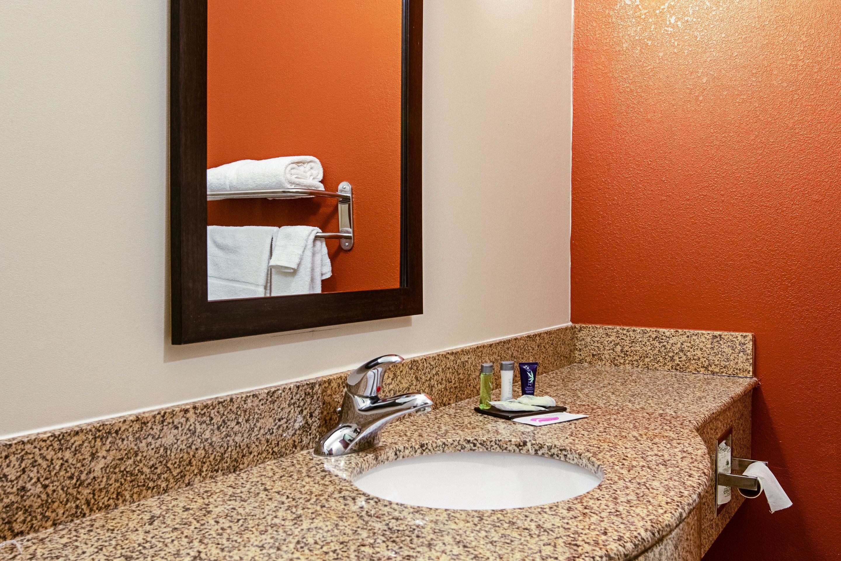 A bathroom with a granite countertop, a white sink, a mirror, and a towel rack with folded towels.