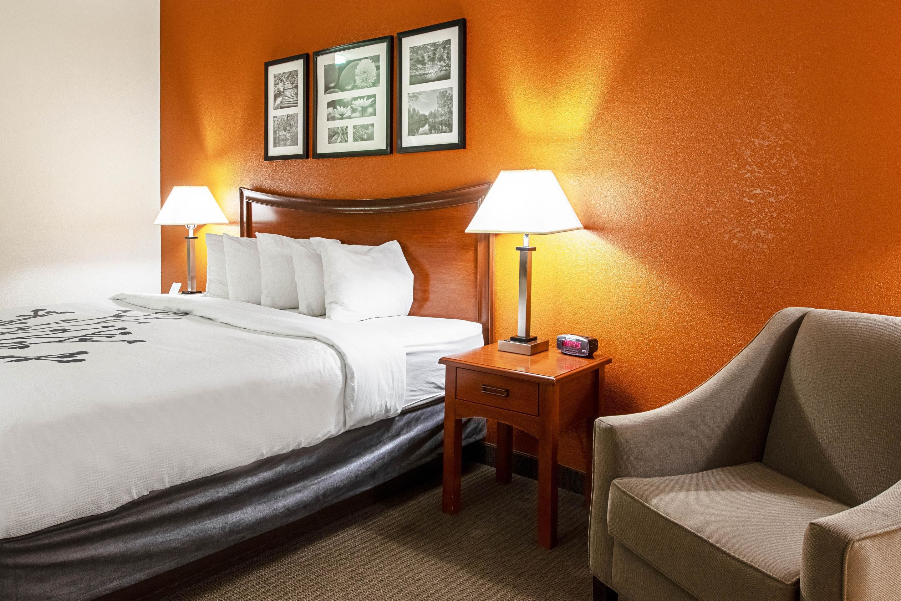 A hotel room with a large bed, two bedside tables with lamps, a chair, and framed pictures on the wall.