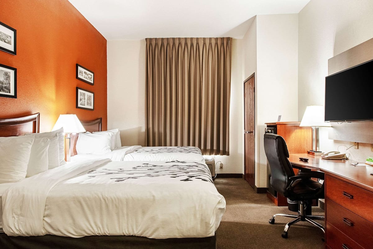 A hotel room with a bed, desk, chair, TV, and curtains.