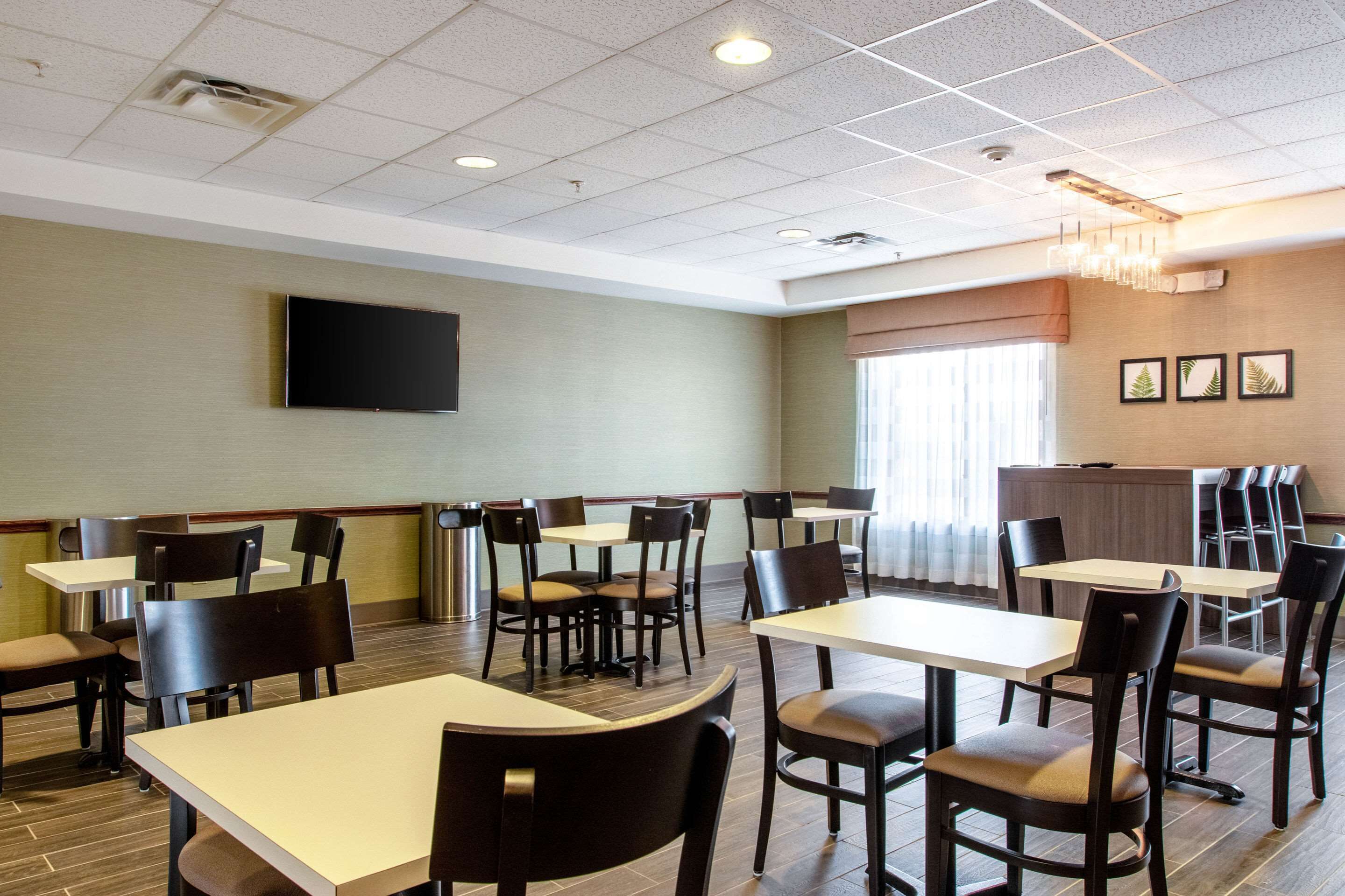 Une salle à manger d’hôtel avec plusieurs tables et chaises, un téléviseur à écran plat fixé au mur et un lustre.