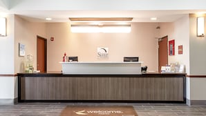 Un comptoir d’accueil avec une enseigne indiquant « Sleep Inns & Suites », un écran numérique et un paillasson.