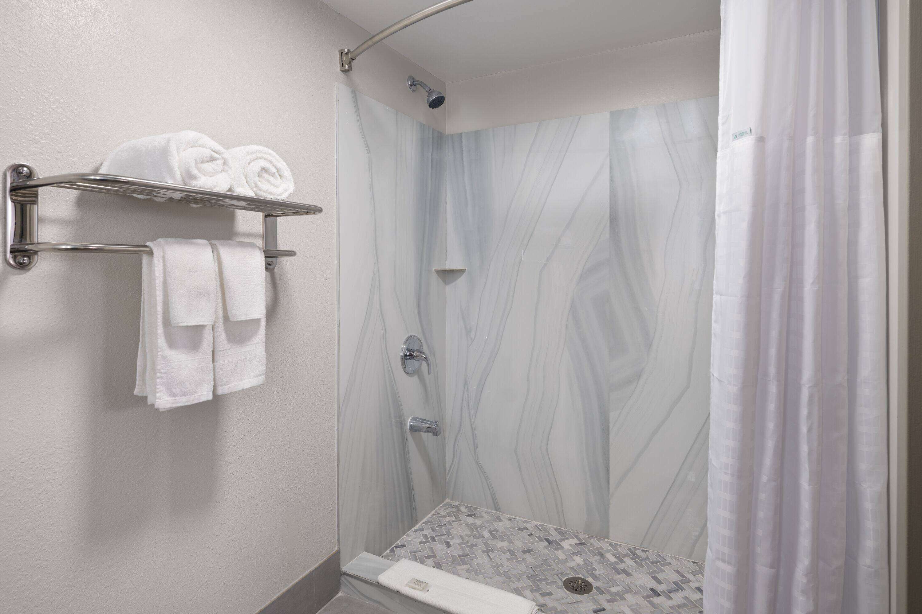Eine Dusche mit Marmorwand, einem Handtuchhalter mit gefalteten Handtüchern und einem Duschvorhang.