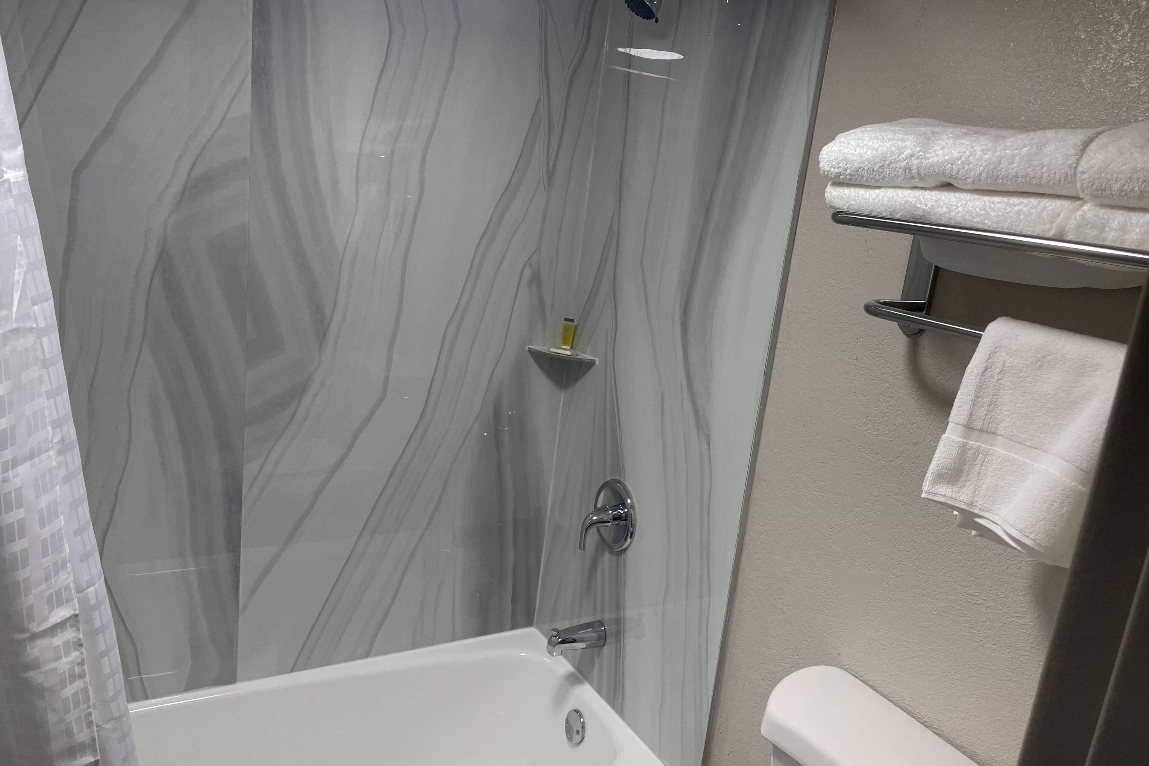 Une salle de bain avec un mur de douche en marbre, une baignoire blanche et un porte-serviettes avec des serviettes pliées.