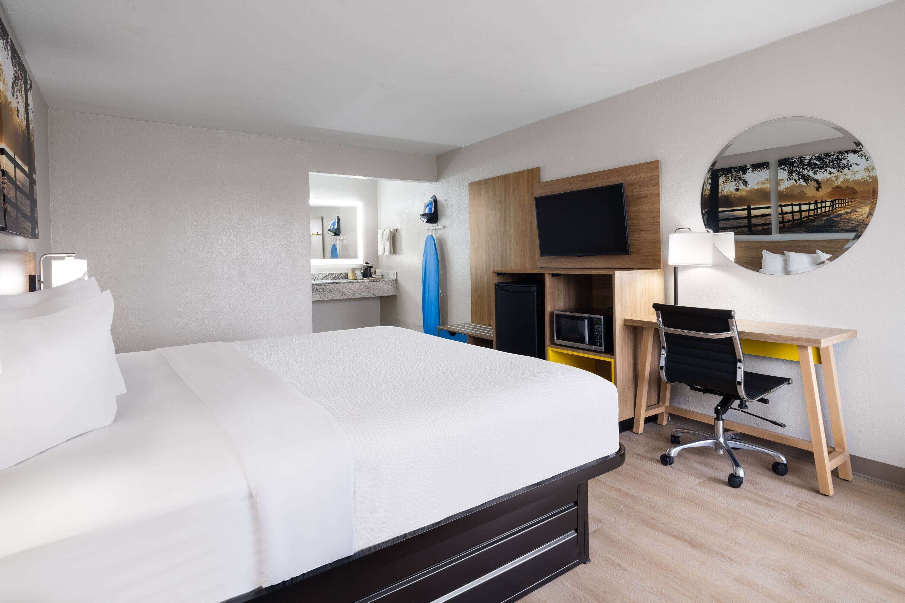 A hotel room with a large bed, a desk with a chair, a TV, a mirror, and a round mirror on the wall.