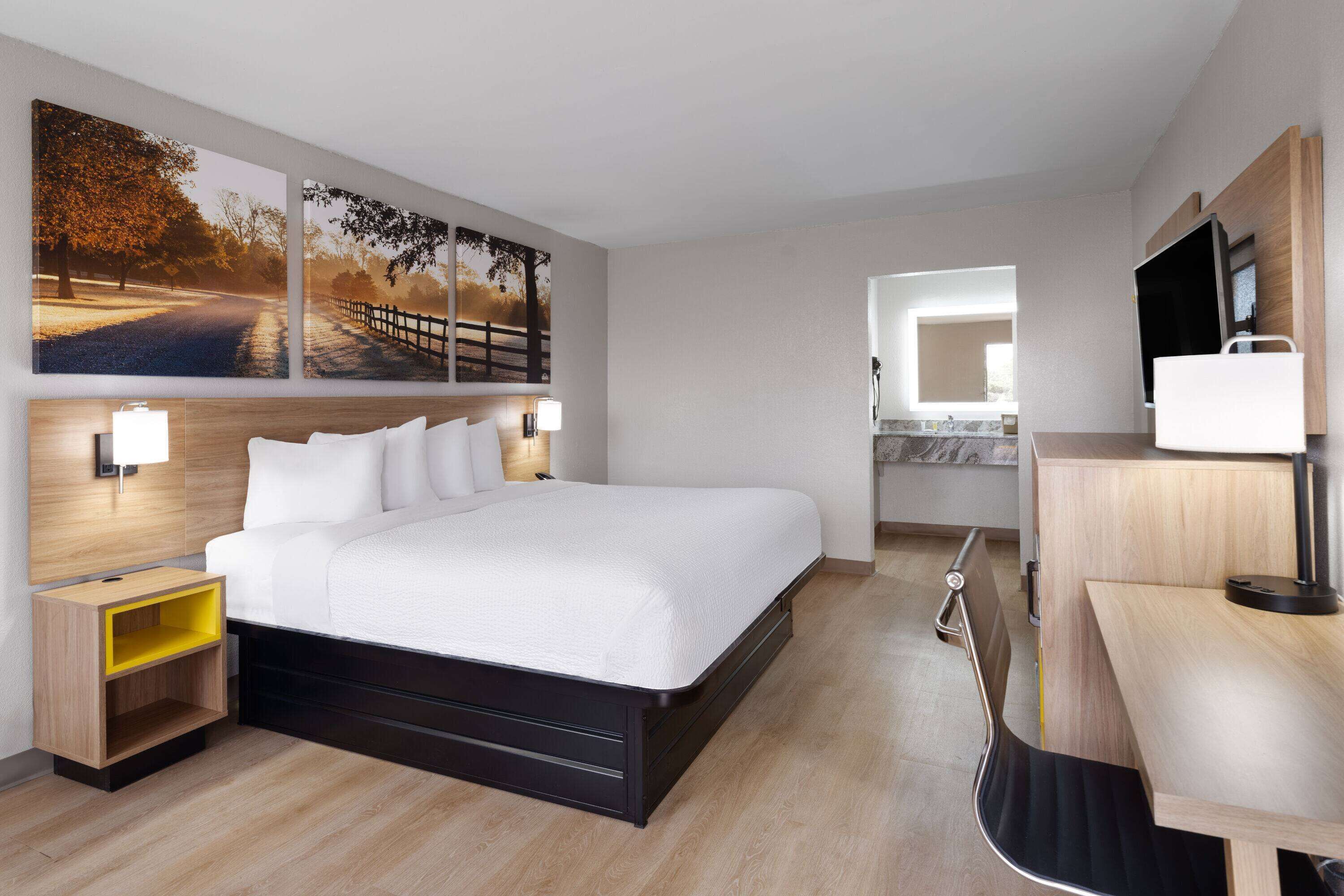 A modern hotel room with a large bed, bedside tables, a desk, and a TV.