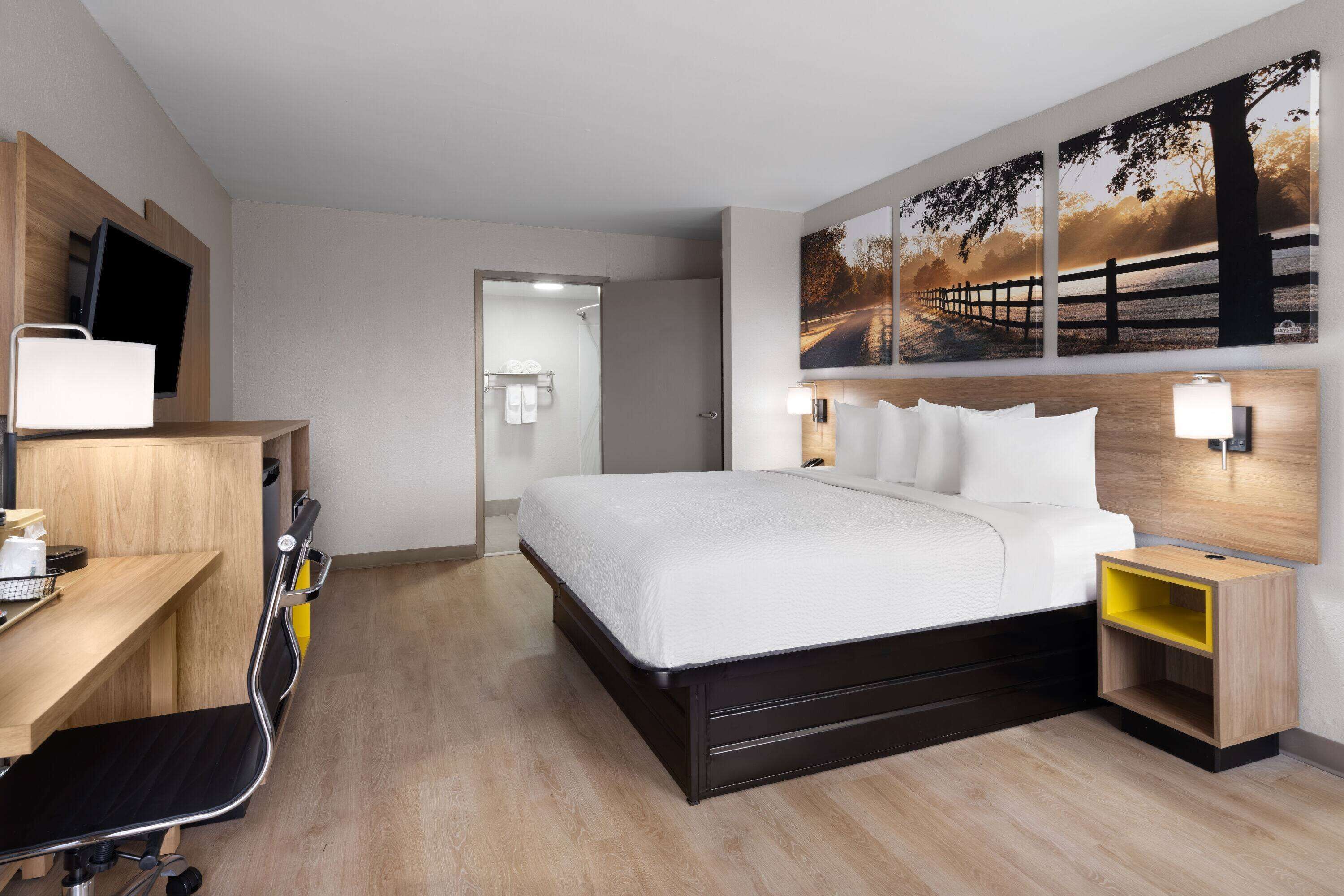 A modern hotel room with a large bed, a desk with a chair, a TV, and a painting on the wall.