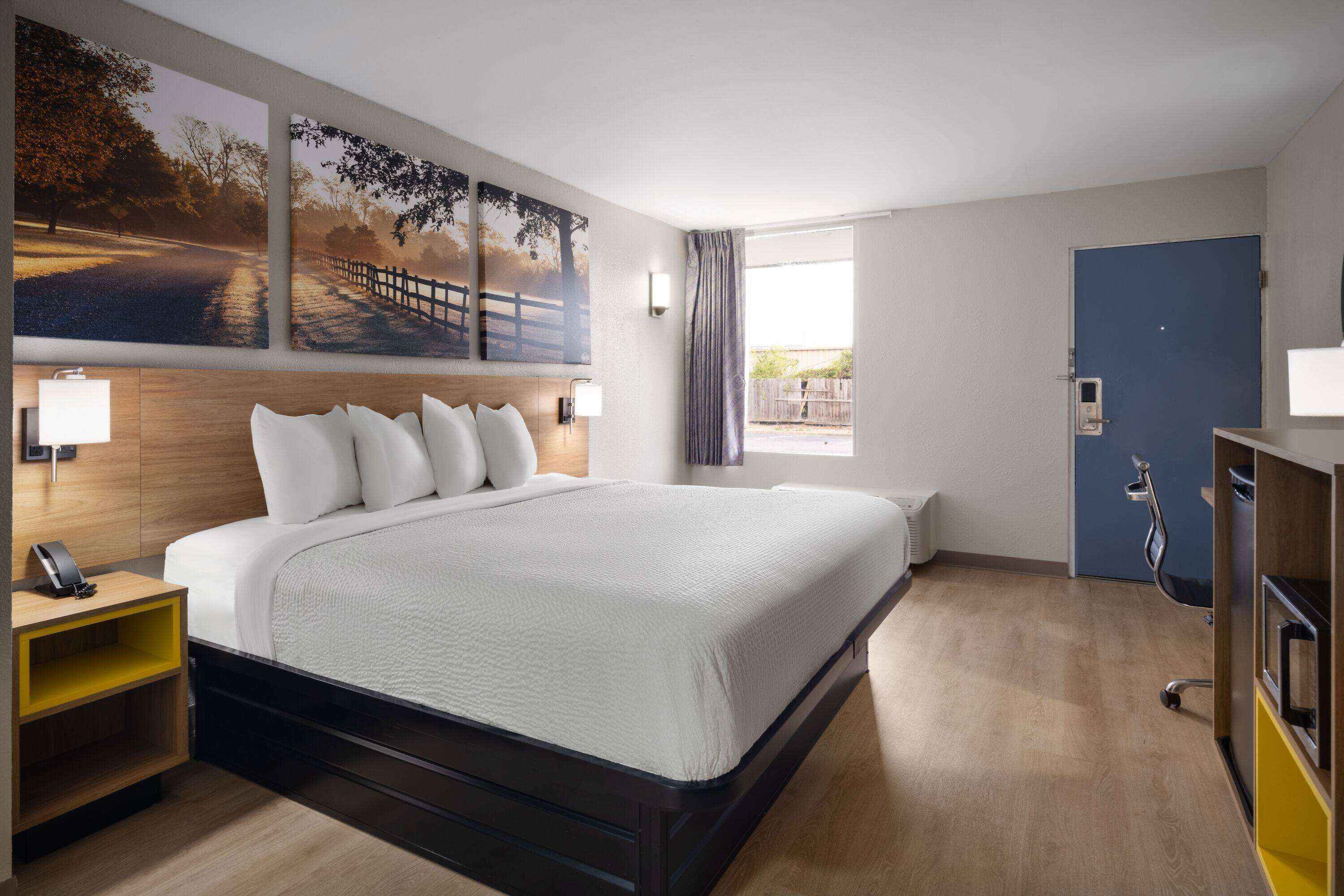 A modern hotel room with a large bed, a bedside table with a lamp, a wardrobe, and a window with curtains.