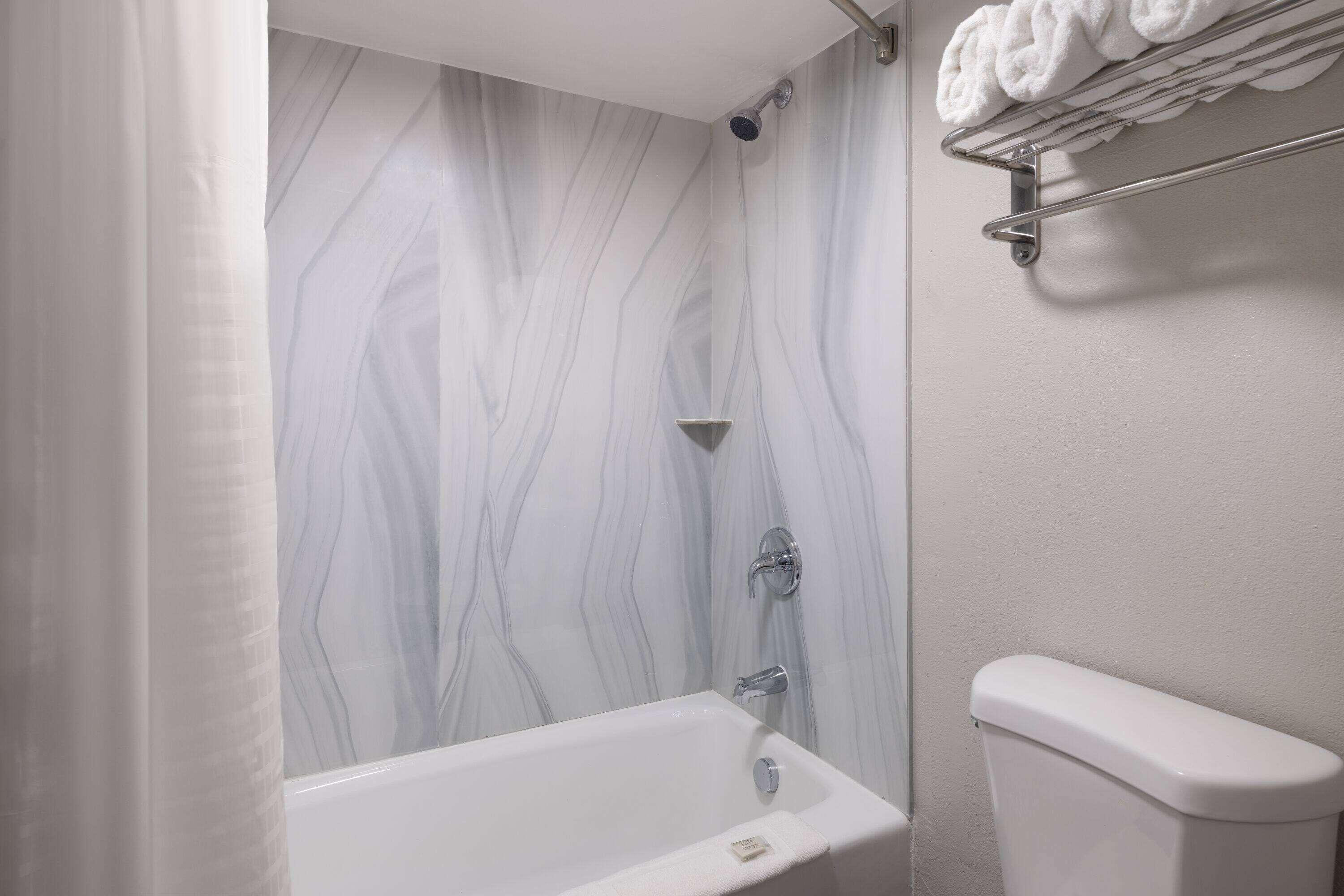 A bathroom with a marble-patterned wall, a bathtub, a toilet, and a towel rack with rolled towels.