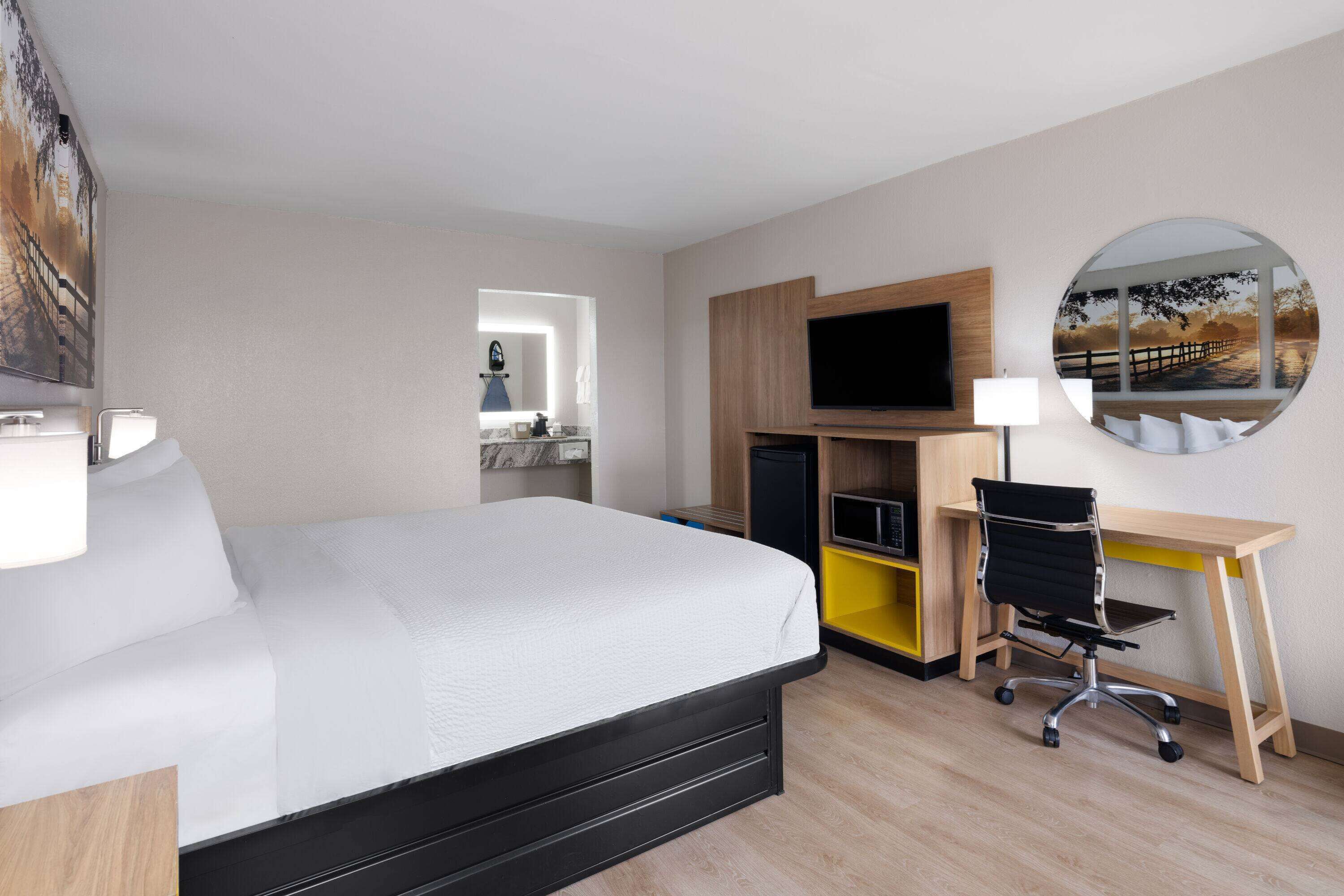 Een hotelkamer met een bed, een bureau, een stoel, een televisie en een spiegel.