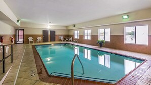 Una piscina interior con agua cristalina, rodeada de suelo de baldosas y una escalera metálica.