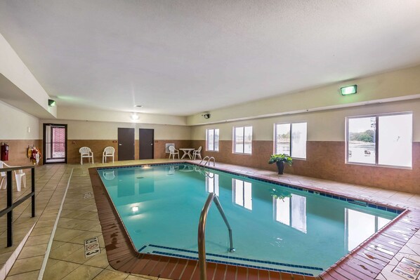 An indoor swimming pool with clear water, surrounded by tiled flooring and a metal ladder.