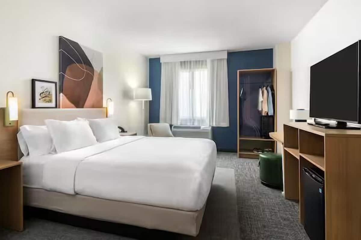 A hotel room with a large bed, bedside tables, a TV, a wardrobe, and a window with curtains.