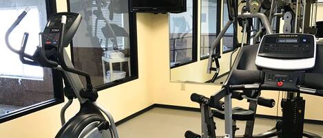 Un gimnasio con equipo cardiovascular, máquinas de pesas y una televisión montada en la pared.