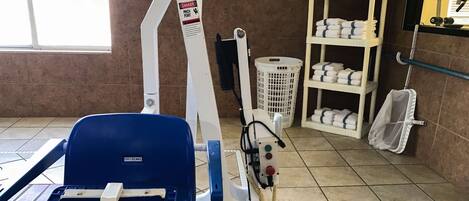 A room with a blue chair, a white shelf with towels, and a white laundry basket.