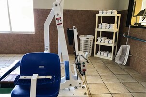 Una habitación con una silla azul, un estante blanco con toallas y un cesto de ropa blanca.